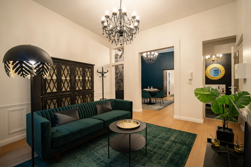 Salon élégant avec canapé vert foncé, meuble noir raffiné, plante décorative et lustre design sur parquet clair.